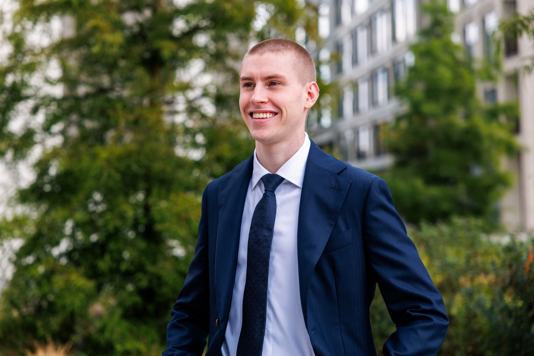 Jérôme glimlacht en kijkt opzij, tussen het groen en de gevels van de stad.